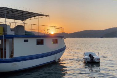 Dağın arka planında, açık havada teknelerle denizde gün batımı