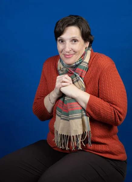 Woman in an orange sweater in the studio. High-quality photo was taken on a blue background with a campy pose.