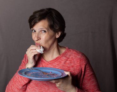 Older woman with an empty blue plate. High-quality photo showing a woman eating a heart-shaped cake. 
