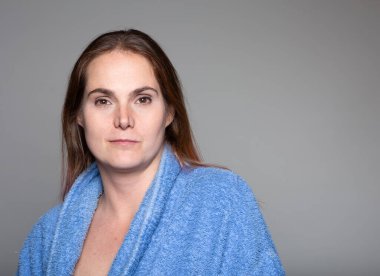 Samimi mavi bornozlu, kendinden emin orta yaşlı bir kadın kamerayla doğrudan göz teması kurar, sakin ve memnun bir aura yayar..