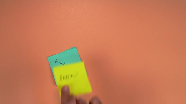 双赢和快乐的文字写在粘贴的字条上 高品质的4K镜头 一个男人的手放置粘贴的笔记在一个苍白的橙色背景 积极成果概念 — 图库视频影像
