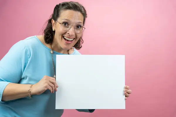 色彩斑斓背景下身穿蓝色衬衫的成熟女商人举着一个标牌 上面有复制的空间 图库照片