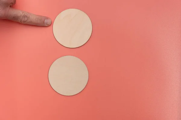Two blank wooden disks with mans finger pointing to top disk on a light pink background with room for copy