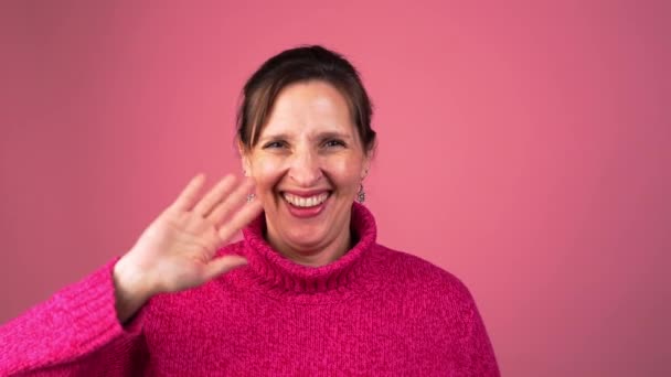 Μια Χαμογελαστή Μεσήλικη Γυναίκα Χαιρετάει Την Κάμερα Στο Στούντιο Ροζ — Αρχείο Βίντεο