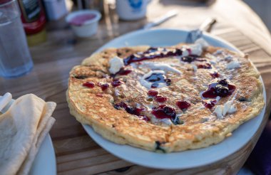 Üstünde yaban mersini şurubu olan bir tabak krep. Krepler altın sarısı ve lezzetli görünüyor.