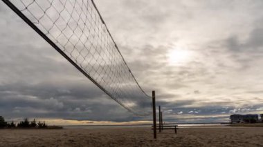 Bir voleybol ağı bir plaj boyunca gerilmiştir. Gökyüzü bulutlu ve güneş zar zor görünüyor.