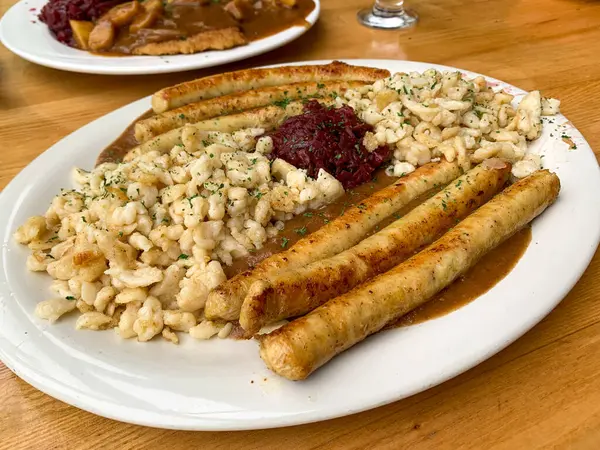 A plate of German food with chicken bratwurst sausages, potatoes, and Red Cabbage on white plate in natural light