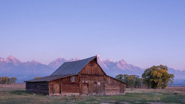 Arka planda dağlar olan bir tarlada kırsal bir ahır var. Gökyüzü mavinin güzel bir tonu.