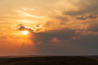 Güneş gökyüzünden batıyor. Gökyüzü bulutlu ve güneş bulutların arasında parlıyor.