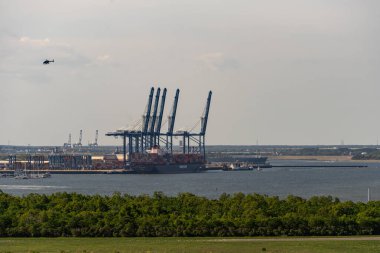 Charleston, SC USA - 30 Nisan 2025 - Güney Carolina Limanı 'ndaki bir yükleme iskelesinde bulunan Hapag-Lloyd konteynır gemisi - Hugh K. Leatherman Terminali puslu bir günde tepemizde helikopterle