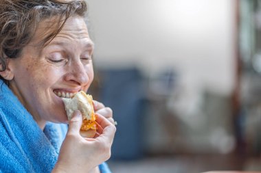 Orta Yaşlı ve Boyutlu Kadın Evde Rahatlarken Kahvaltı Sandviçi Keyfini Çıkartıyor