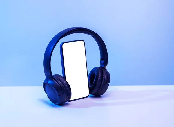 蓝牙耳机智能手机 蓝色霓虹灯背景上有白色屏幕 用于模拟和记录 图库照片
