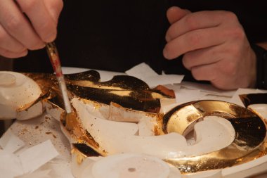 Sanatçı süsü gerçek altınla süslemiş. Kuyumcu. Eller ve fırça