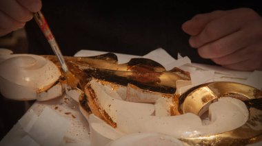 Sanatçı süsü gerçek altınla süslemiş. Kuyumcu. Eller ve fırça