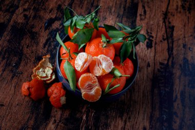 Eski ahşap bir masanın üzerinde mavi bir seramik tabakta yaprakları olan Clementines.