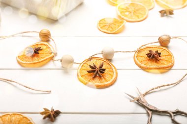 Kurumuş portakal dilimlerinden yapılmış Noel dekoru ve beyaz ahşap arka planda anason.