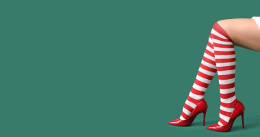 Yeşil arka planda Noel çoraplı seksi genç kadın bacakları ve mesaj için yer.