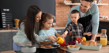 Genç ve mutlu bir aile mutfakta birlikte yemek pişiriyor.