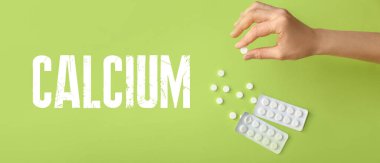 Yeşil arka planda kalsiyum hapları olan bir kadın el.