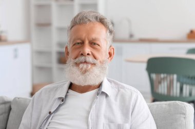 Mutfakta koltukta oturan yaşlı sakallı adam, yakın plan.