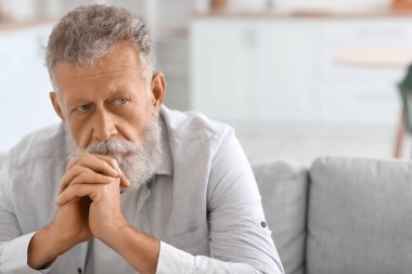 Mutfakta koltukta oturan düşünceli kıdemli adam, yakın plan.