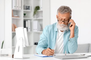 Ofiste cep telefonuyla konuşan ve yazı yazan kıdemli bir adam.