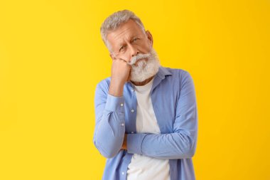 Sarı arka planda düşünceli olgun bir adam.