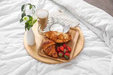 Kahvaltı tepsisi, yatak odasındaki beyaz battaniye üzerinde kahve ve çiçekler.