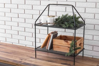 Noel dalları, mumlar ve beyaz tuğla duvarın yanında kitapları olan raf ünitesi.