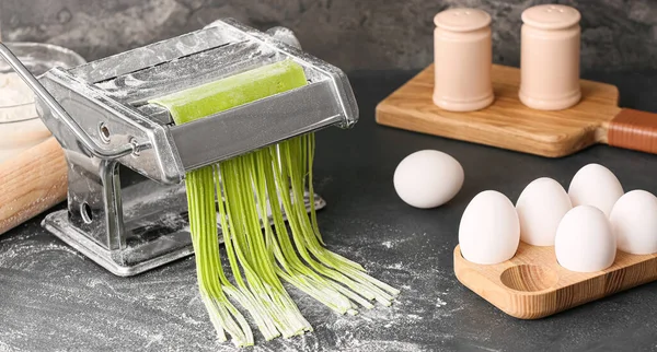 Pasta machine with green noodles and ingredients on table