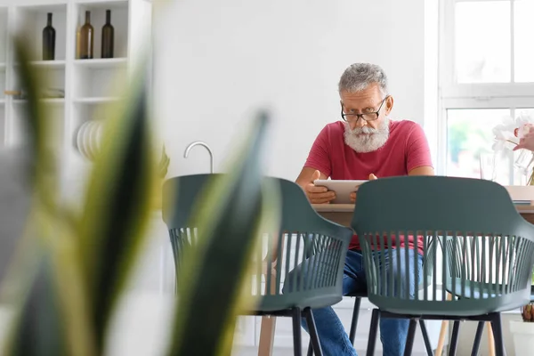 stock image Senior man using tablet computer at table in kitchen