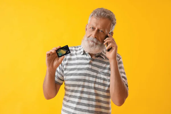 有信用卡的老年人在黄色背景下用手机交谈 — 图库照片