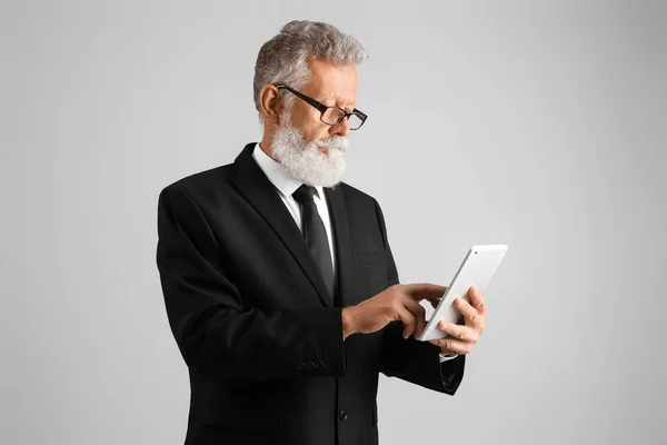 Senior man in suit using tablet computer on grey background