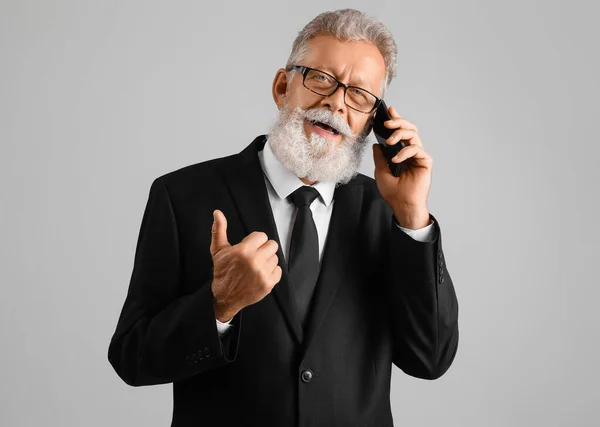 Senior man in suit talking by mobile phone on grey background
