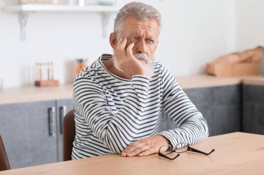 Mutfakta masada oturan düşünceli olgun bir adam.