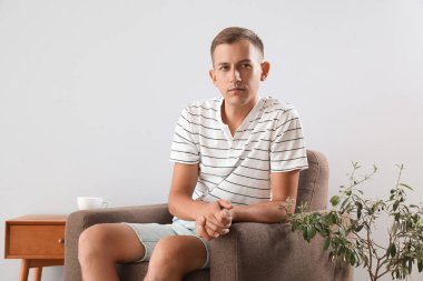 Genç adam ışık duvarının yanındaki yumuşak koltukta oturuyor.