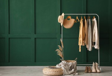 Örgü süveterler, aksesuarlar ve yeşil duvarın yanında ayakkabılar.