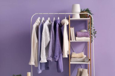 Renkli duvarın yanında örülmüş süveterler ve raf ünitesiyle dizin.