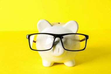 Sarı arka planda gözlüklü domuz kumbarası. Bütçe kavramı