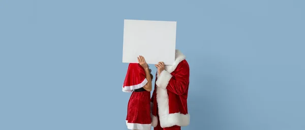 Young Couple Santa Costumes Holding Blank Poster Light Blue Background — Stock Photo, Image