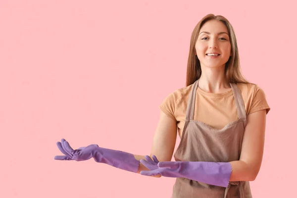 戴橡胶手套的年轻女人指着粉色背景的东西 — 图库照片