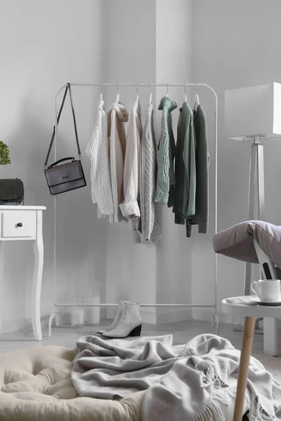 stock image Rack with knitted sweaters, bag and shoes in light living room