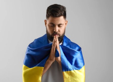 Ukrayna bayrağı taşıyan genç adam gri arka planda dua ediyor.