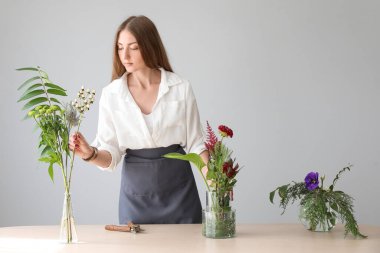 Gri duvarın yanındaki masada güzel bir ikebana yapan genç kadın.