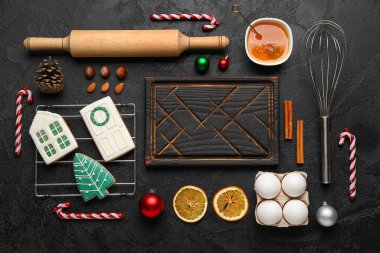 Koyu arkaplanda Noel kurabiyeleri hazırlamak için ahşap kesim tahtası ve malzemeleri olan kompozisyon