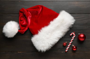Koyu ahşap arka planda Noel süsleri olan Noel Baba şapkası