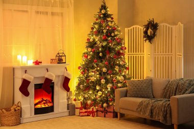 Oturma odasının içinde Noel ağacı, şömine ve parlayan ışıklar var.
