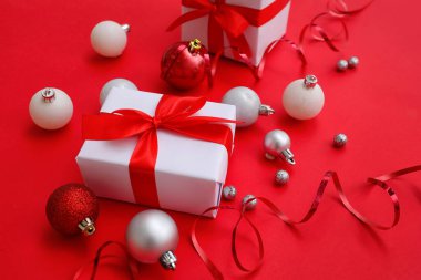 Kırmızı arka planda Noel hediyeleri, toplar ve yılan var.