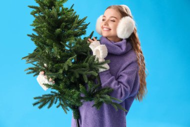 Mavi arka planda Noel ağacı olan genç bir kadın.