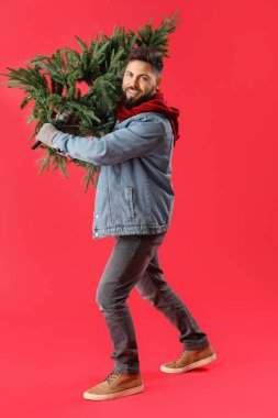 Kırmızı arka planda Noel ağacı olan yakışıklı bir adam.